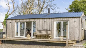 Une cabane en bois avec un toit en métal, de grandes fenêtres et un banc à l’extérieur.