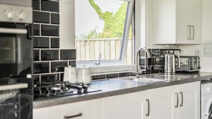 Une cuisine moderne équipée d’une cuisinière à gaz, d’un évier, d’une fenêtre donnant sur un espace verdoyant et de meubles blancs.