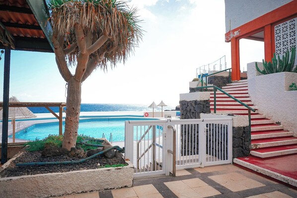 A poolside area with a palm tree, a staircase with red steps, and a view of the ocean.