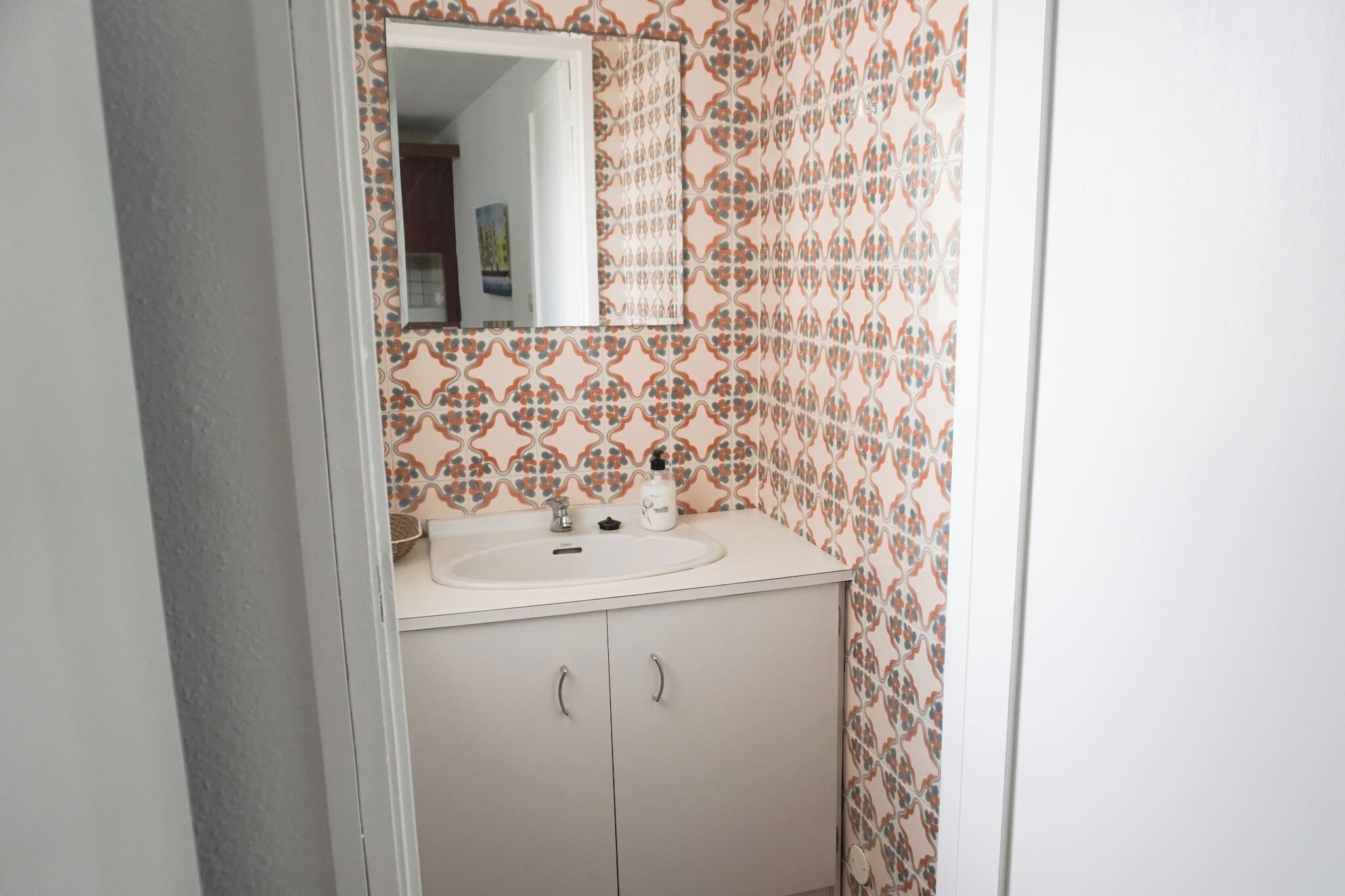 Een badkamer met een wastafel, spiegel en behang met een patroon.