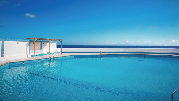 Uma piscina azul límpida com um pergolado de madeira e vista para o oceano.