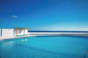 A clear blue swimming pool with a wooden pergola and a view of the ocean.