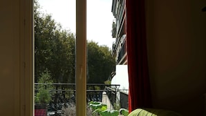 A room with a green sofa, a red curtain, and a view of a building and trees outside.