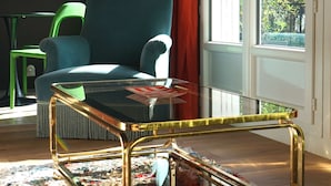 A room with a teal armchair, a glass-top coffee table, and a colorful rug.
