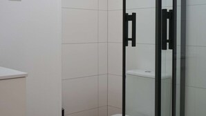 A modern bathroom with a glass shower enclosure, a white toilet, and a wooden floor.