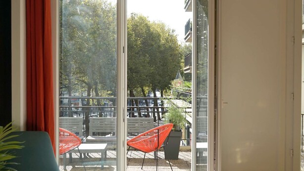 A room with a green sofa, a red chair, and a glass table.