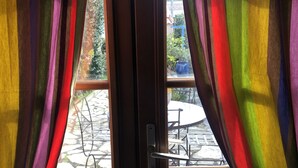A view through a window with curtains, revealing an outdoor patio area with stone flooring and outdoor furniture. - Studio Equipe a Proximite Plages et Commerces (Six-Fours-les-Plages)