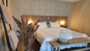 Ein Hotelzimmer mit Bett, Nachttisch, Lampe und einer Vase mit Trockenblumen.