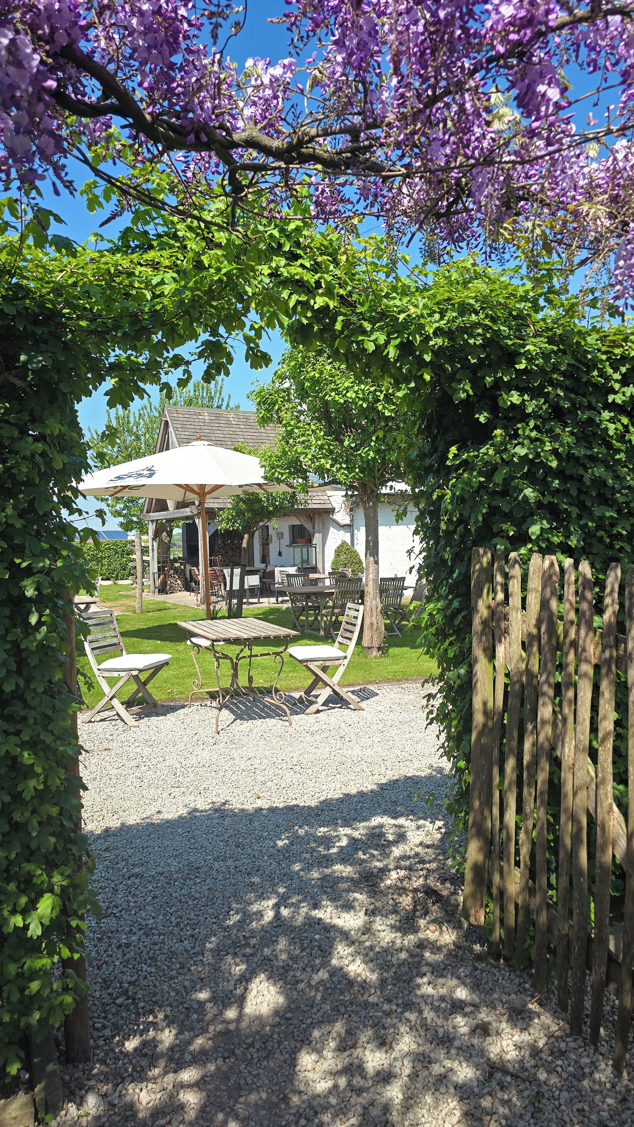 Un patio con mobiliario exterior, una pérgola y vistas a una casa con chimenea de piedra.
