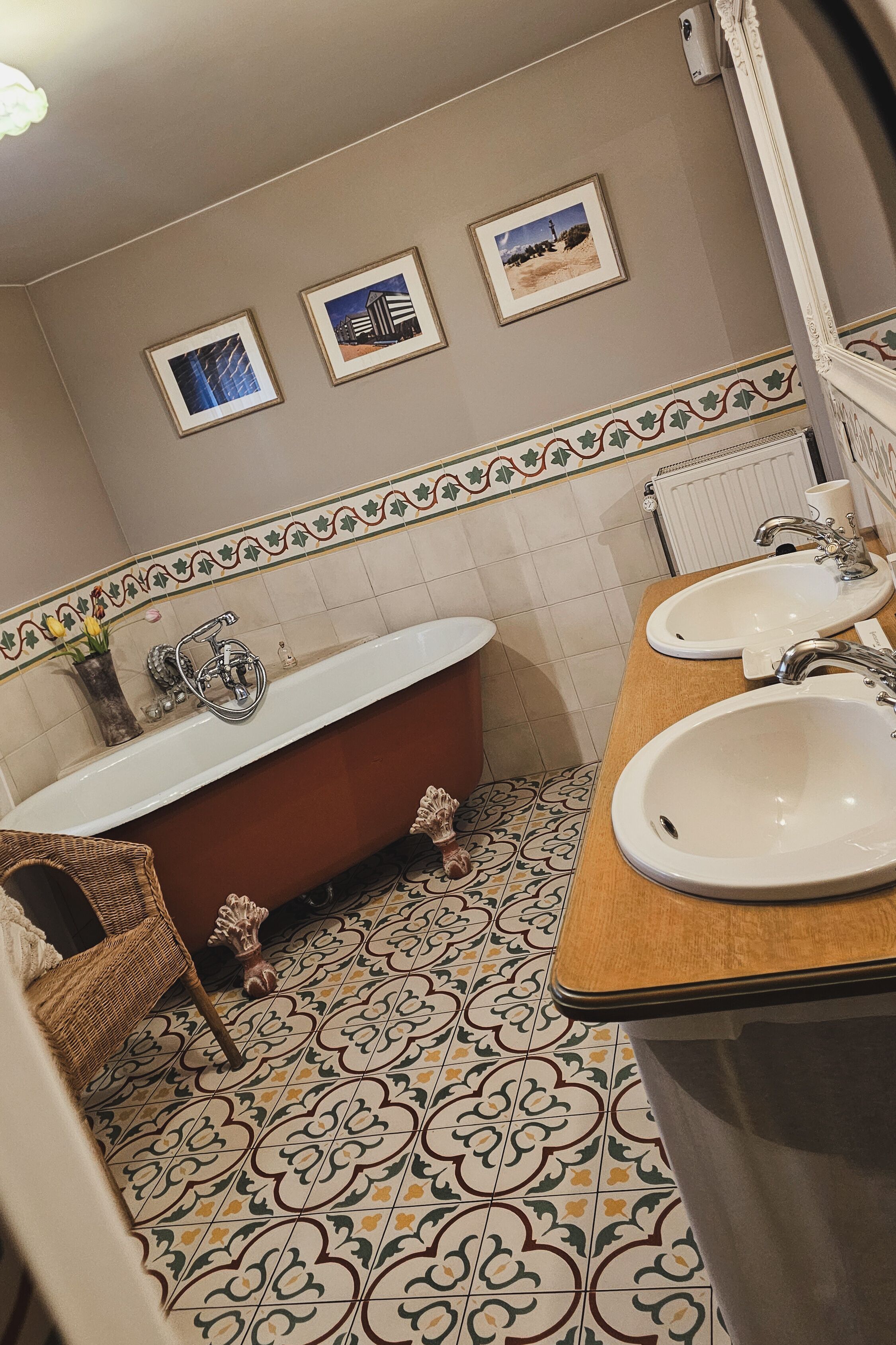 Une salle de bain avec une baignoire sur pieds, deux lavabos, des carreaux décoratifs et des tableaux encadrés accrochés au mur.