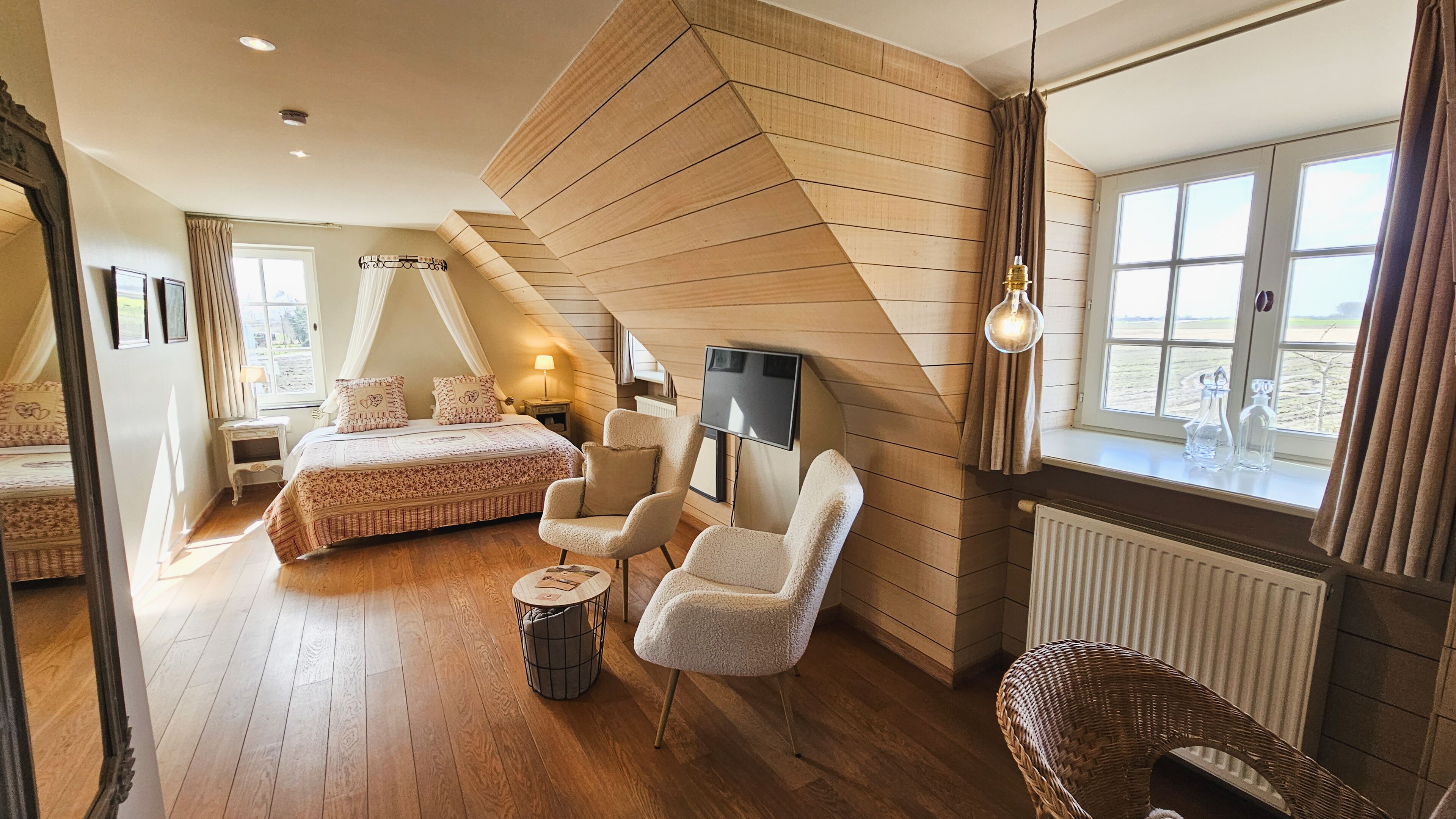 A bedroom with a bed, two chairs, a TV, and a window with curtains.