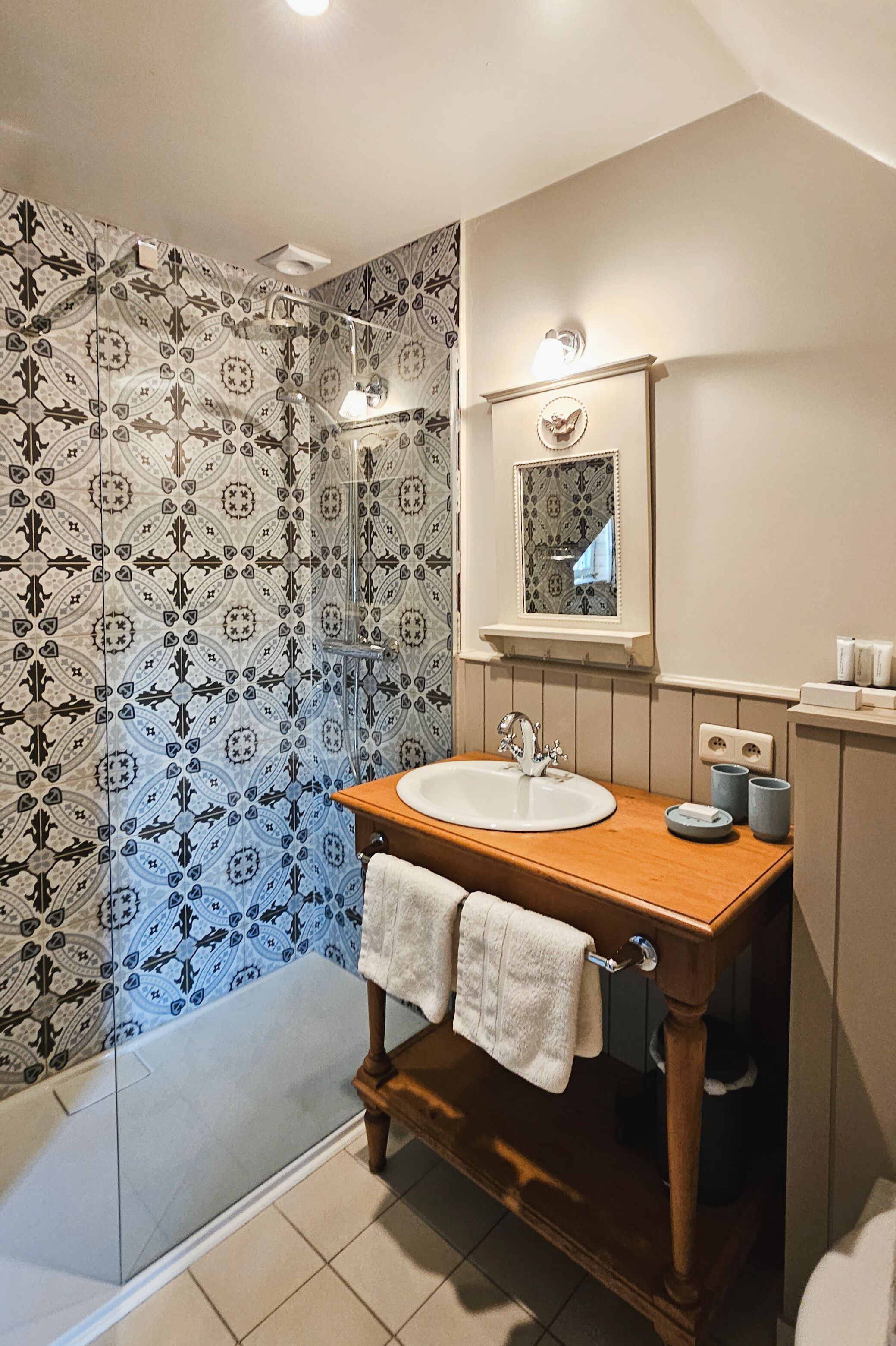 Un baño con cabina de ducha de vidrio, tocador de madera con lavamanos y papel tapiz estampado.