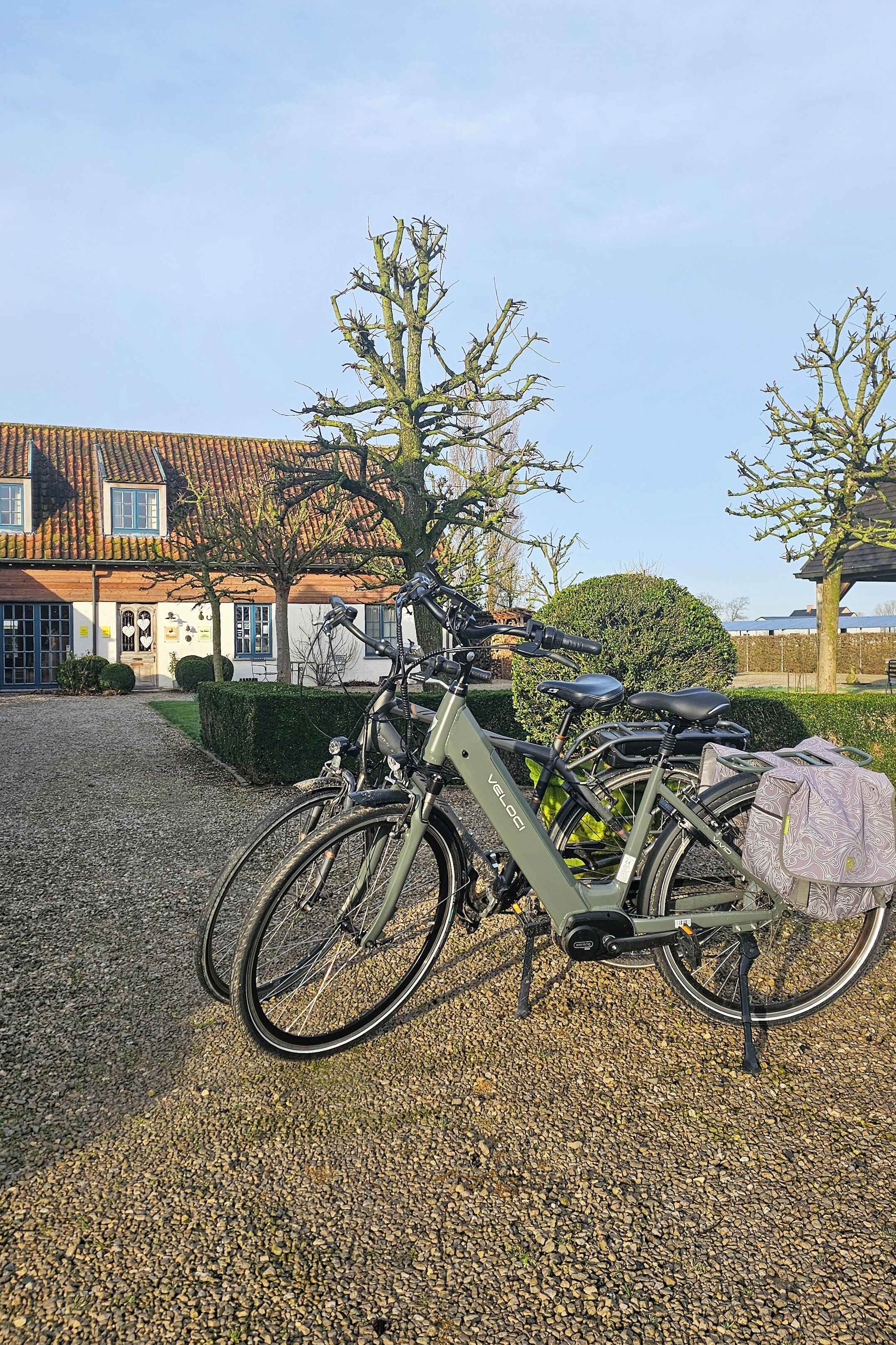 Una bicicletta parcheggiata di fronte a un edificio con tetto in tegole e vialetto sterrato.