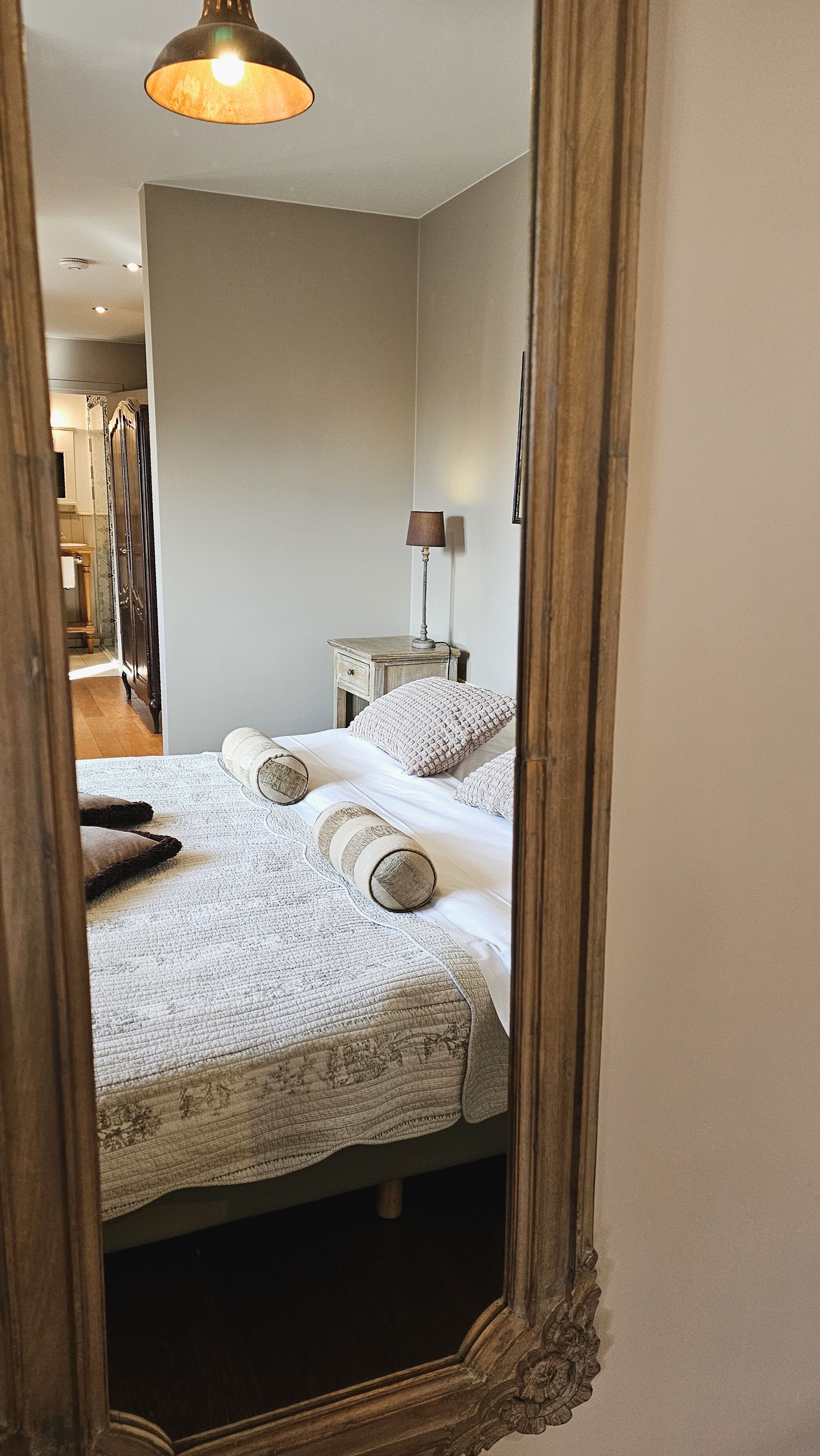 A bedroom with a bed, a nightstand, a lamp, and a mirror.