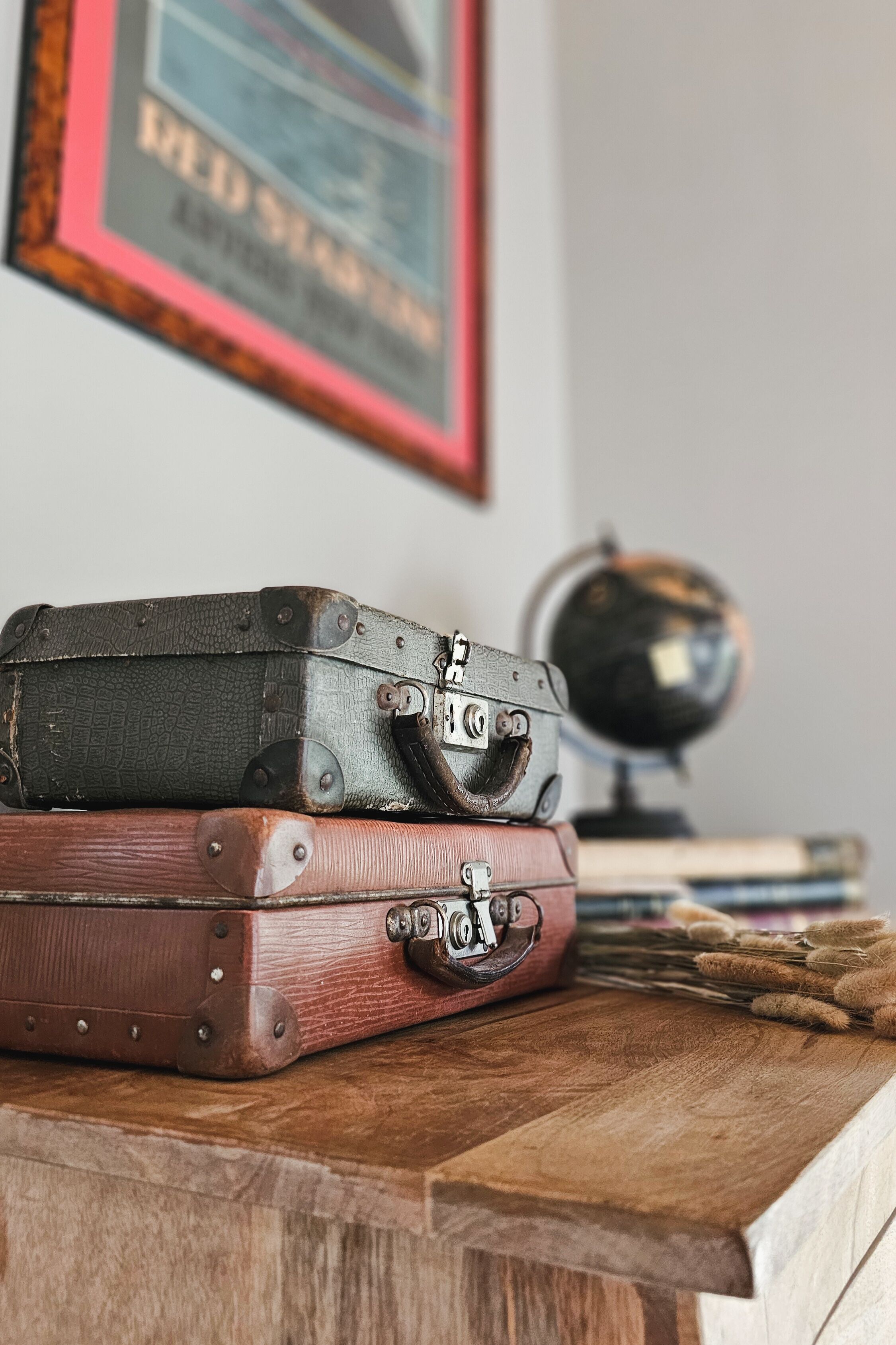 A stack of vintage suitcases on a wooden surface with a globe and books in the background.
