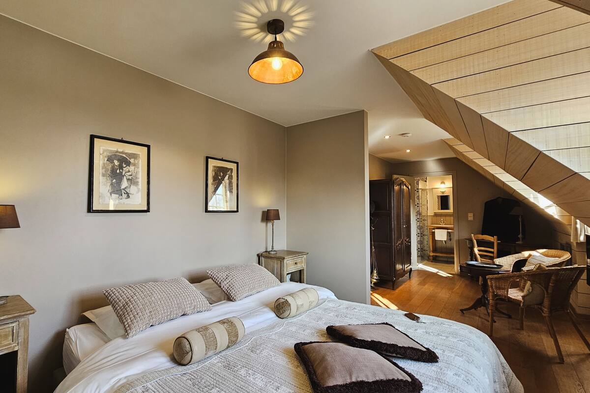 Une chambre dotée d’un grand lit, de deux tables de chevet, d’un luminaire suspendu et d’un escalier menant à un étage supérieur.