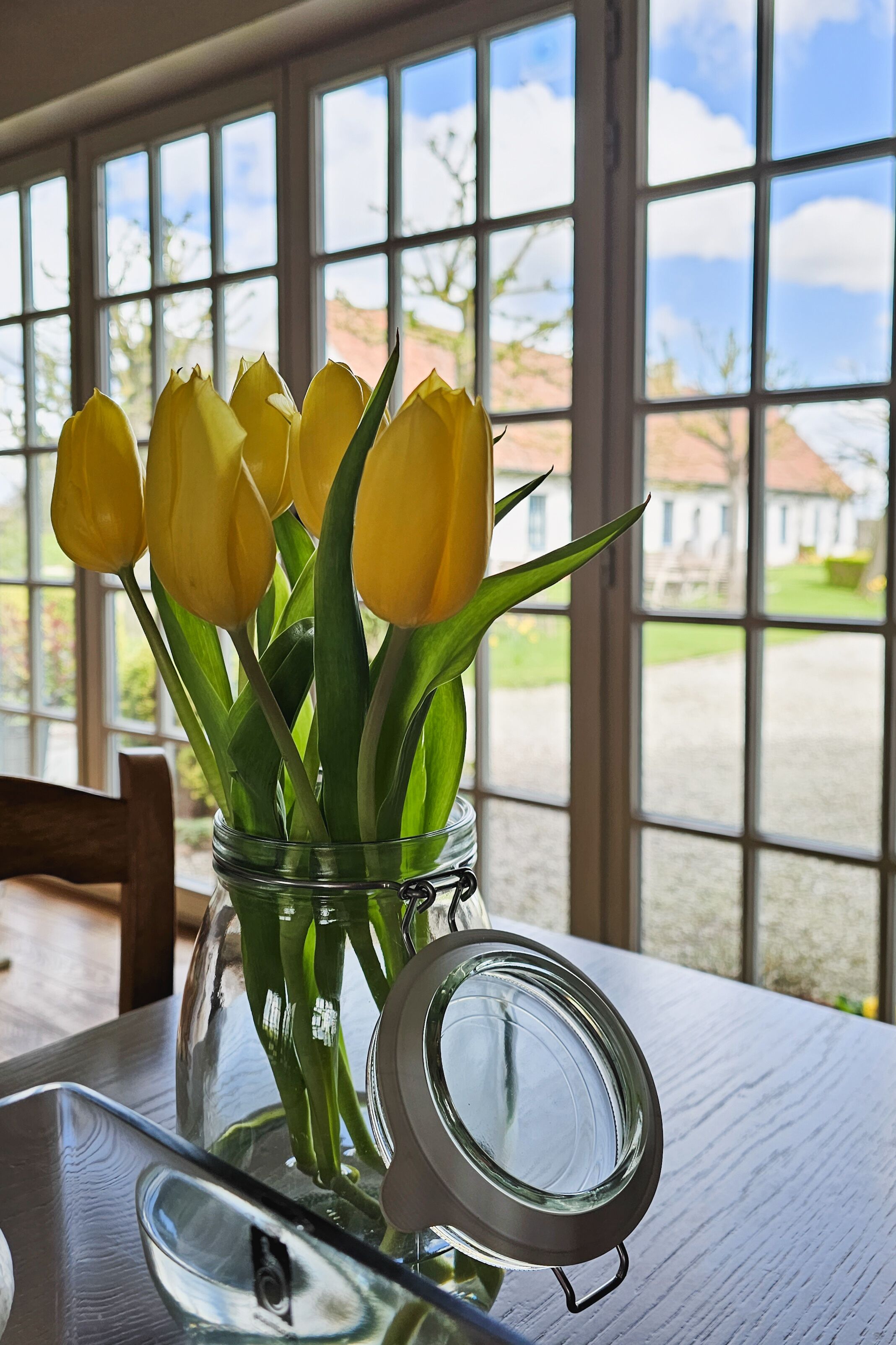 Un tarro de vidrio con tulipanes amarillos sobre una mesa cerca de una ventana.