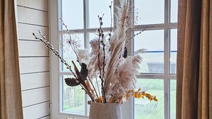 Ein Fenster mit Blick auf einen Garten, eine Vase mit getrockneten Pflanzen und eine kleine Holzschatulle auf dem Fensterbrett.