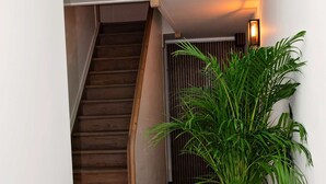 A hallway with a wooden staircase, a large potted plant, and a wall-mounted light fixture. - Modern and Stylish! Luxury apartment for 7 in the center of Antwerp. (Antwerp)