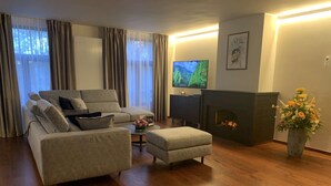 A living room with a sofa, ottoman, TV, fireplace, and a vase of flowers. - Modern and Stylish! Luxury apartment for 7 in the center of Antwerp. (Antwerp)