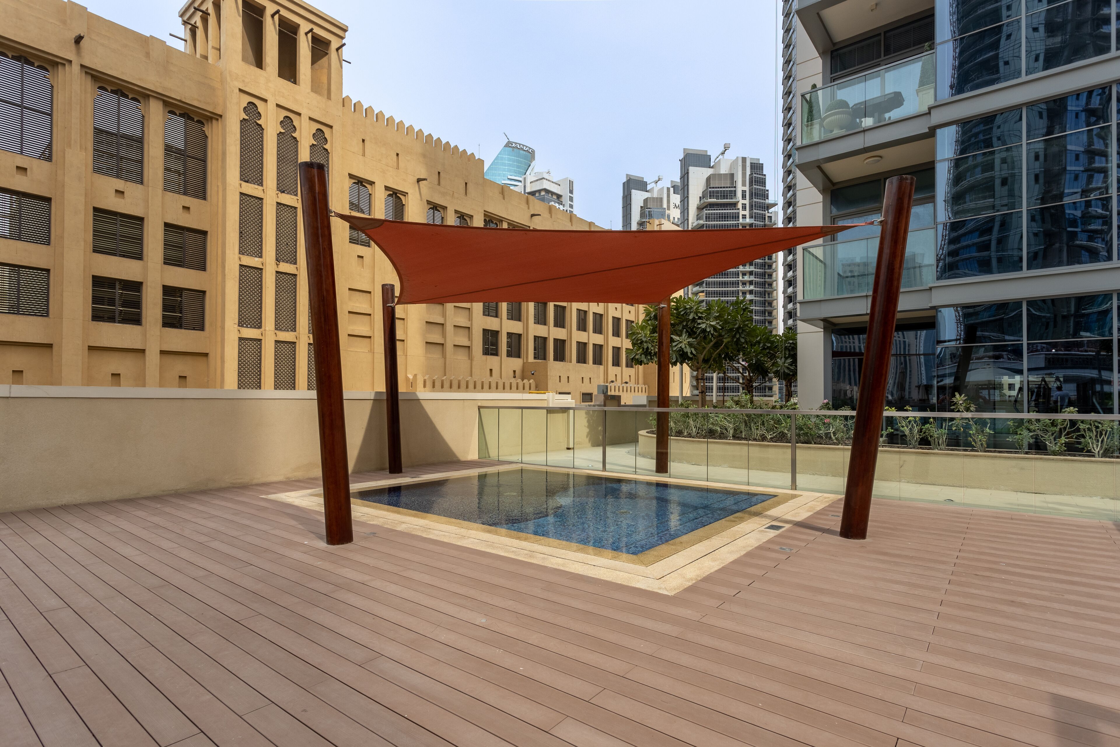 A rooftop pool with a wooden deck and a large shade structure.