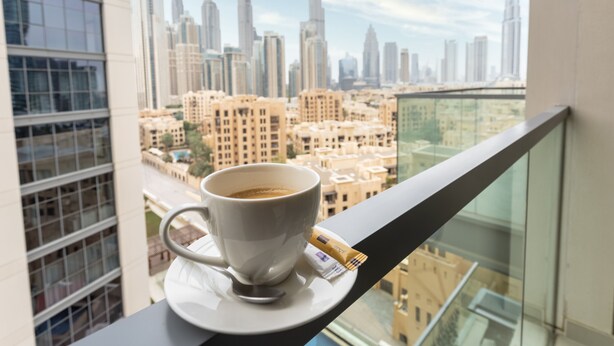 A cup of coffee on a balcony with a cityscape view, including a prominent skyscraper. - Waves - Chic Apartment With Dubai Skyline Views (Dubai)