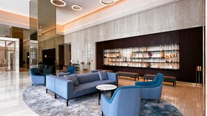 A modern lobby with a sectional sofa, armchairs, and a coffee table. There is a large wall display with decorative items. - Waves - Chic Apartment With Dubai Skyline Views (Dubai)