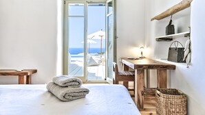 A bedroom with a bed, a wooden desk, a wicker basket, and a view of the sea through a glass door. - VILLA EKAVI FILIZI - Seaside Residence just outside of Naousa (Naousa)