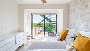 Quarto moderno com uma cama grande, um ventilador de teto e vista para uma escada que dá a uma varanda.