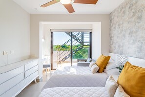 Camera da letto moderna con un letto grande, un ventilatore a soffitto e vista su una scala che porta a un balcone.