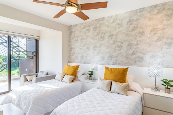 A modern bedroom with two beds, a ceiling fan, and a large window with a view of greenery.