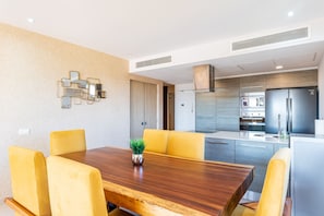 A modern kitchen with stainless steel appliances, a dining area with yellow chairs, and a decorative wall piece.