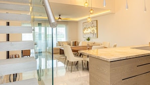 Un interior moderno con una escalera de cristal, un comedor y una isla de cocina.