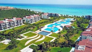 An aerial view of a resort with multiple swimming pools, a large central pool, and a view of the ocean.