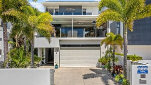 A modern two-story building with a garage door, surrounded by tropical plants. - 100 steps to the beach. Our modern Sunshine Coast home accommodates 12 guests (Alexandra Headland)