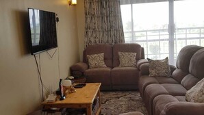 A living room with a sofa set, a television mounted on the wall, and a window with curtains. - 3-bed Apartment in Nanyuki With Golf Course Views (Nanyuki)