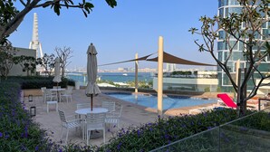 A rooftop pool area with outdoor seating and a view of the city skyline. - Waves - Sea View Luxury 3 Bedroom Apartment With Balcony (Dubai)
