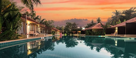 Piscina con agua cristalina que refleja las palmeras y edificios circundantes.
