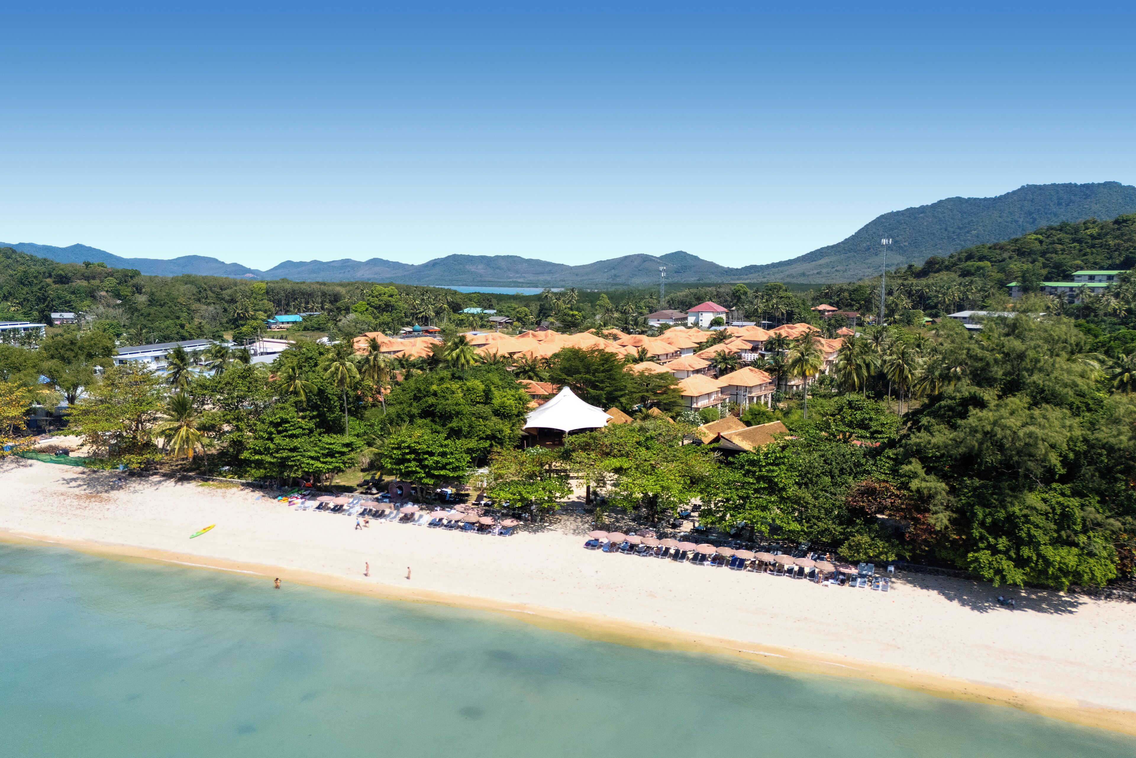 Une station balnéaire située sur la côte, offrant un accès à la plage, des bungalows sur pilotis et un paysage montagneux en arrière-plan.