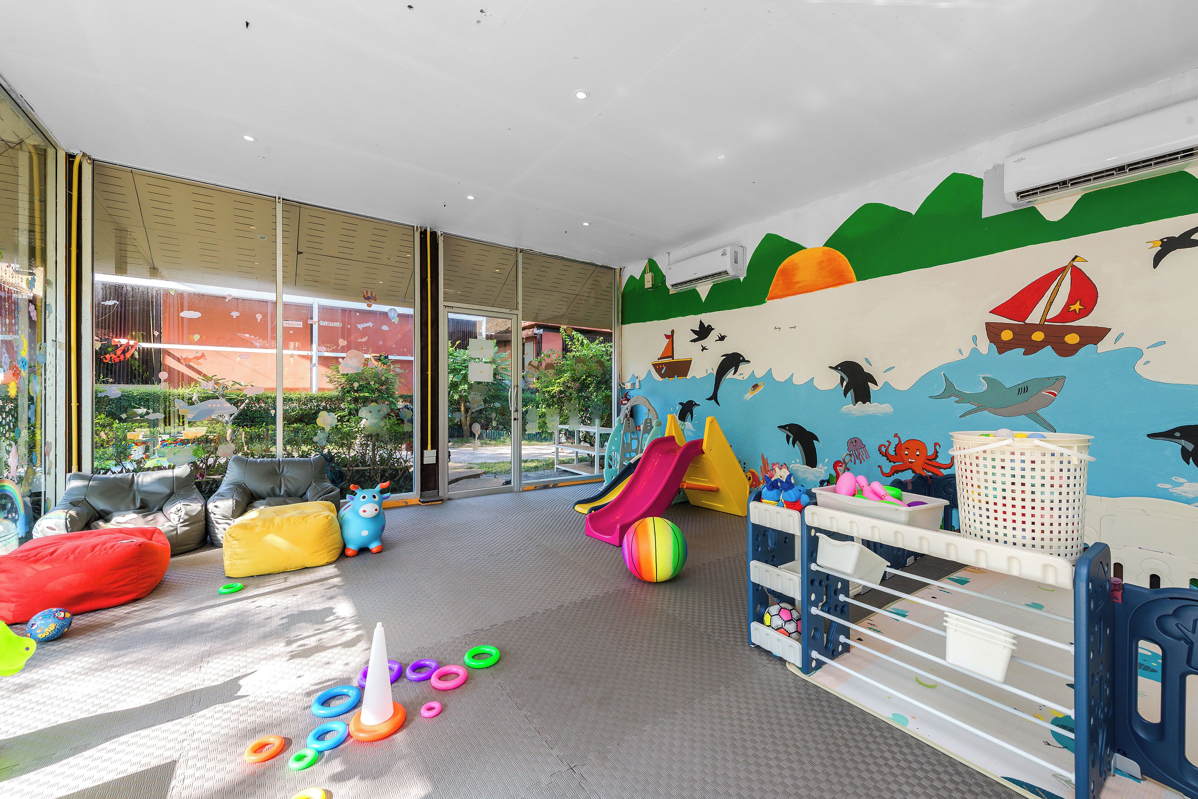 Un espace de jeux pour enfants avec un toboggan, des balles colorées et une fresque murale sur le thème de la plage.