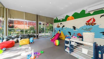 A children's play area with a slide, colorful balls, and a beach-themed mural.