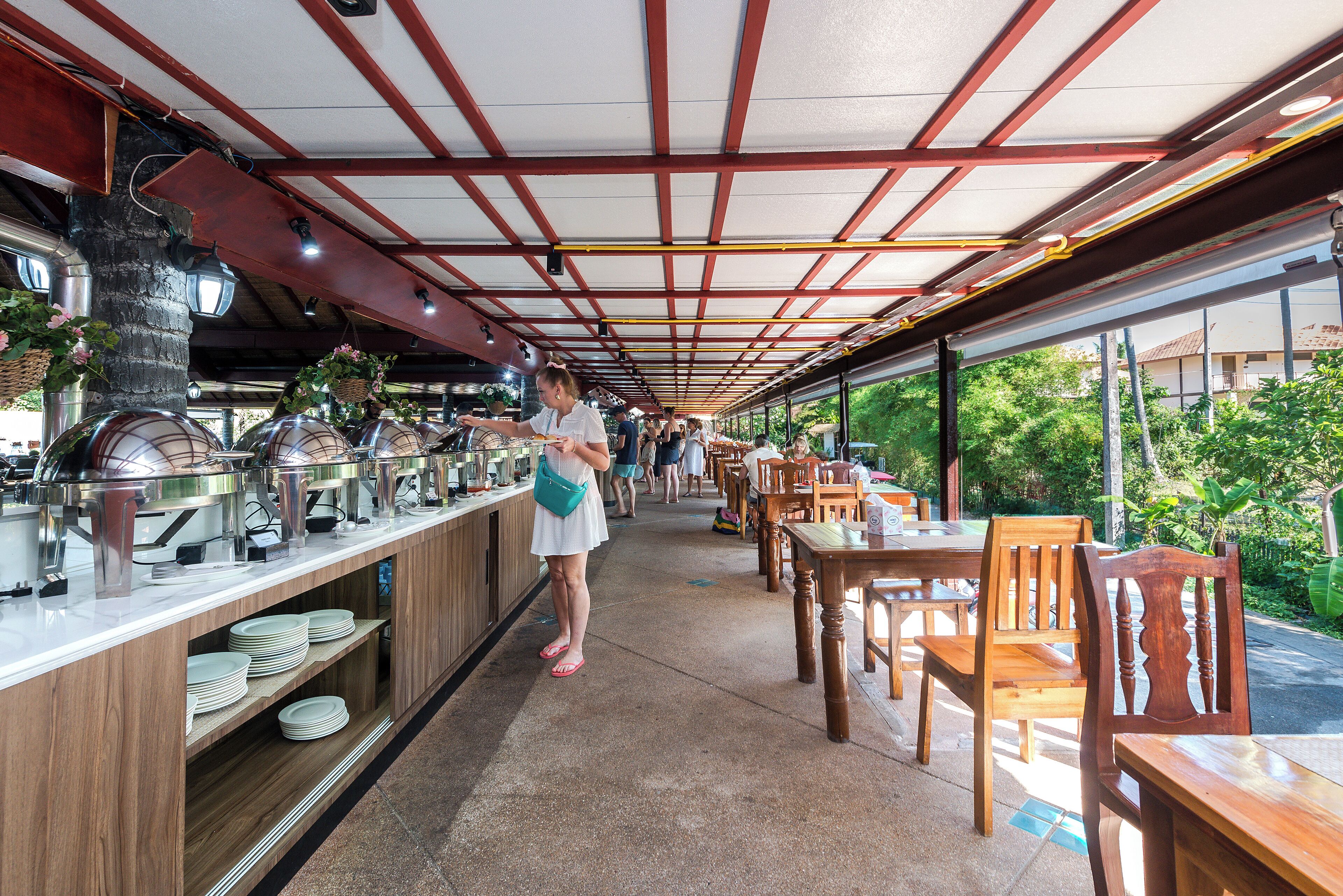 A covered outdoor dining area with buffet counters, wooden tables, and chairs.
