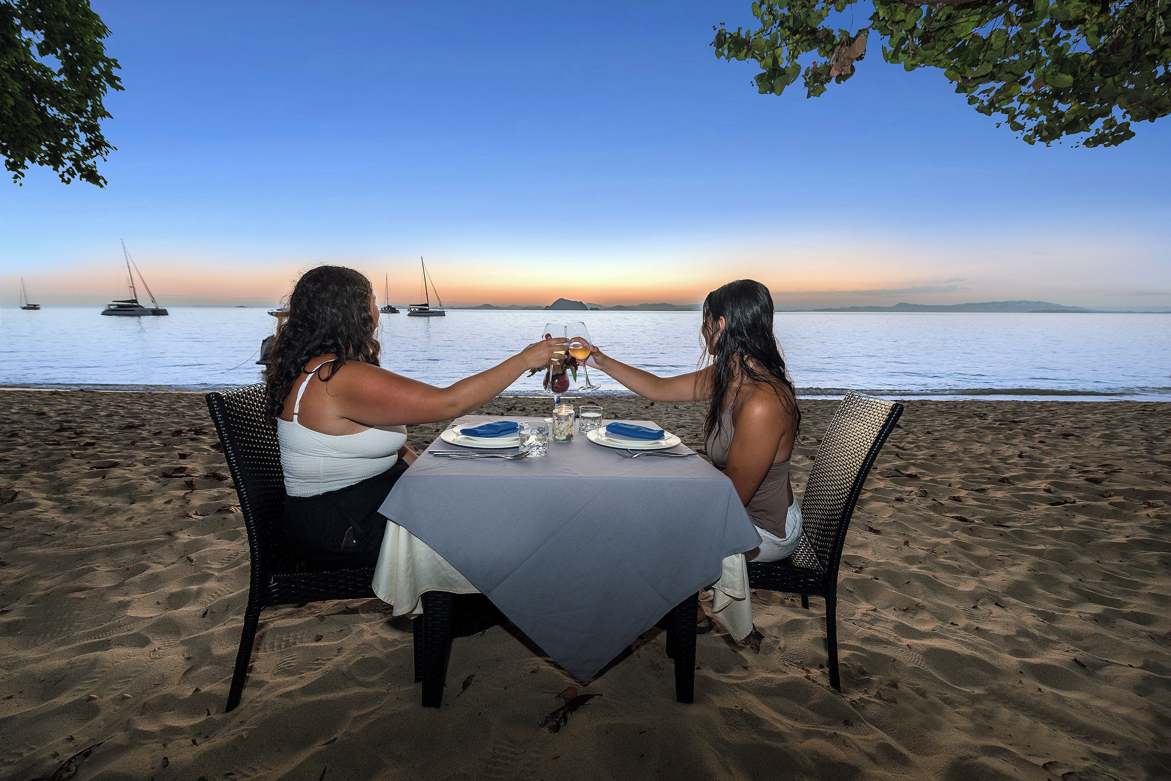 Une table dressée sur une plage de sable, avec vue sur la mer et les bateaux.