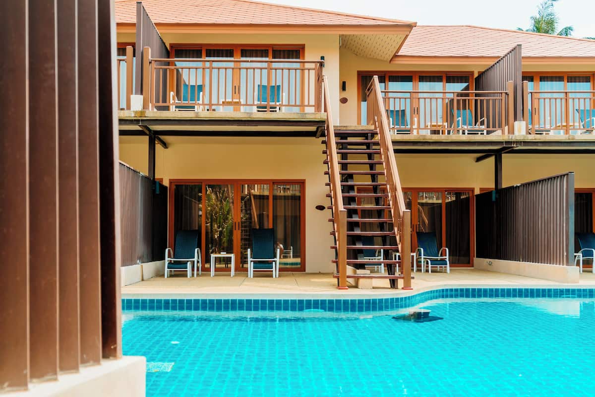A hotel with a swimming pool, a wooden staircase, and multiple balconies with outdoor seating.