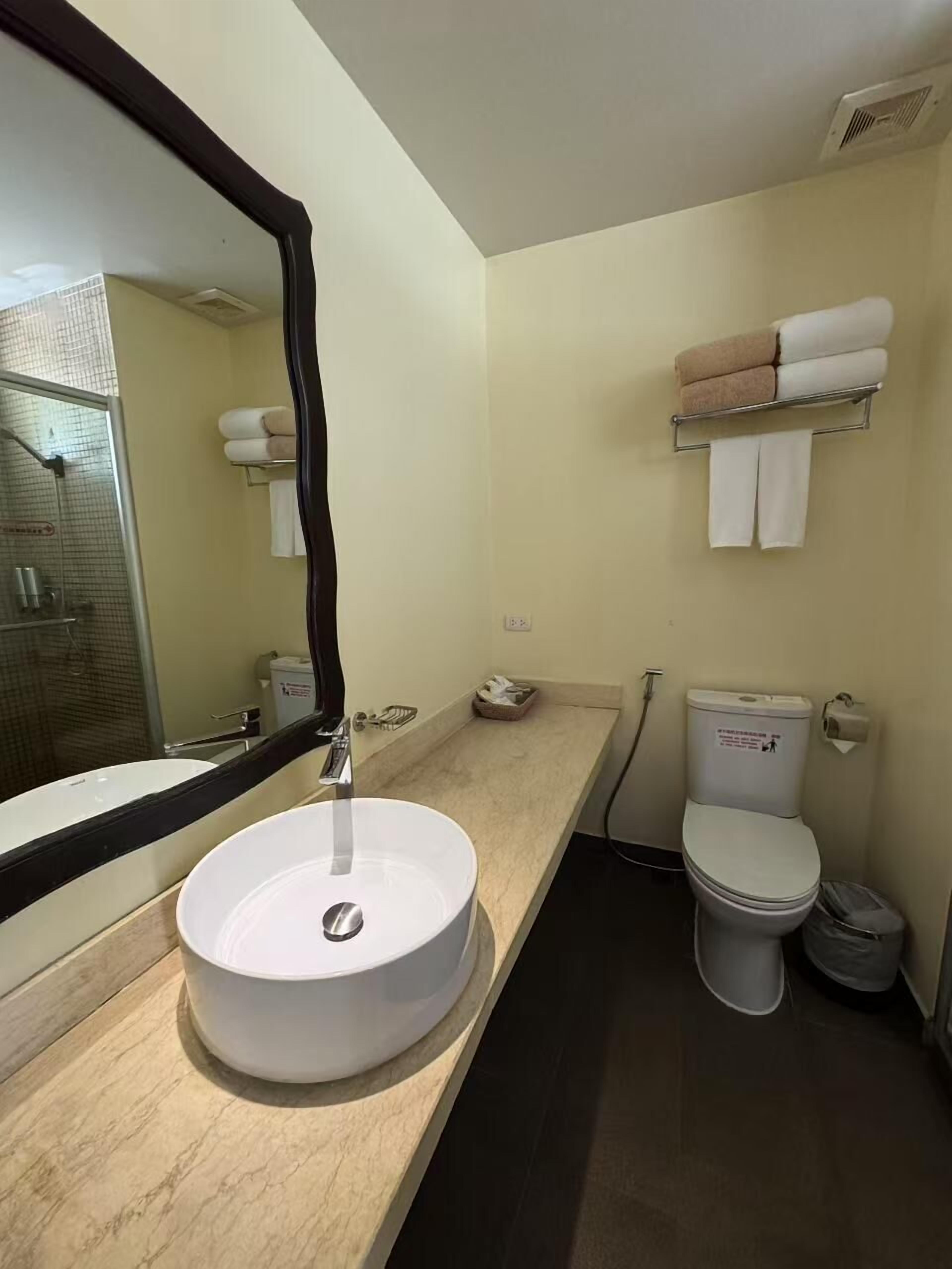A bathroom with a round sink, a toilet, a shower area, and a towel rack with towels.