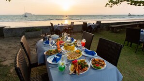 Un área de comedor al aire libre con una mesa dispuesta para una comida, con vista al océano y al atardecer.