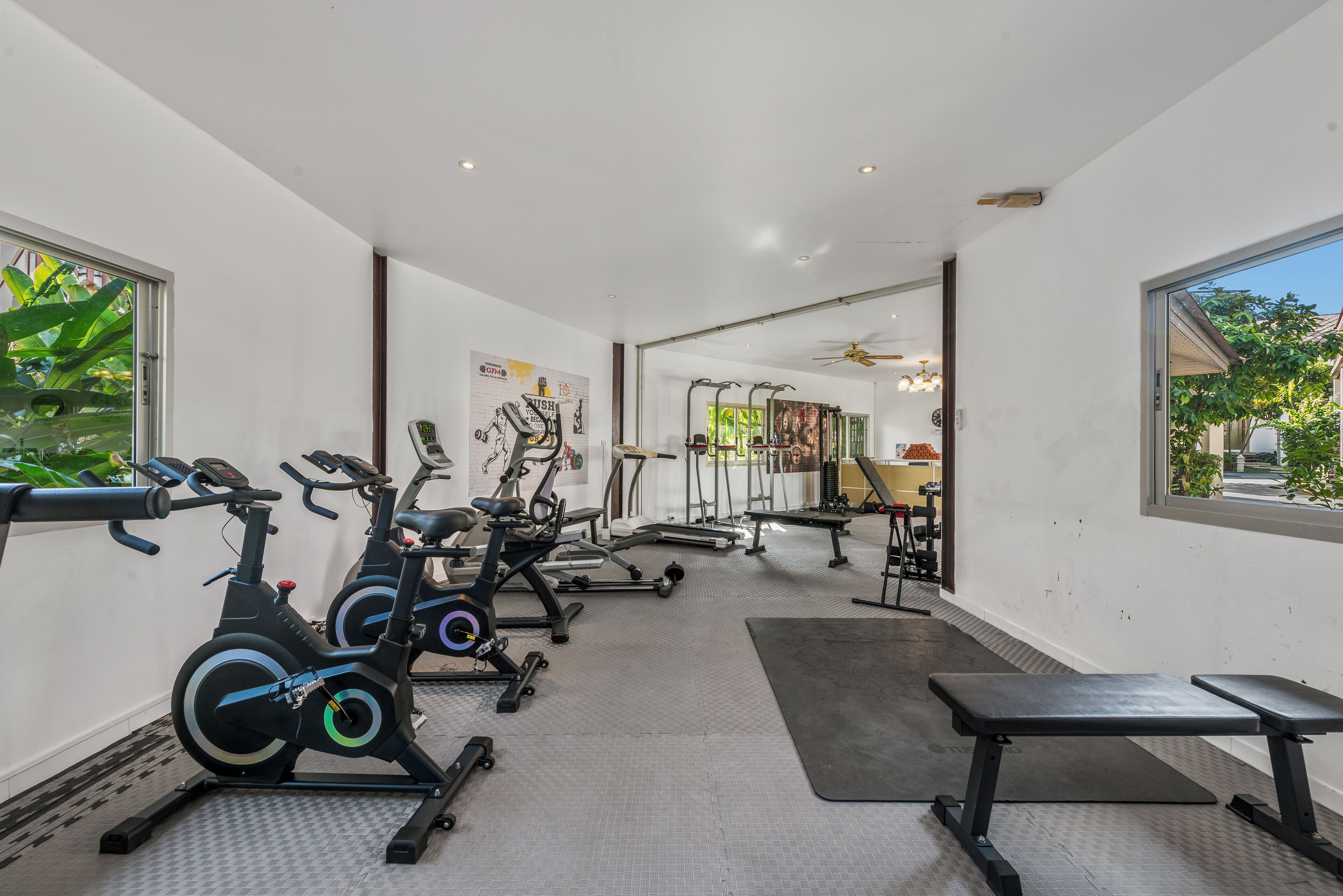 Un gimnasio con equipo de ejercicio, ventilador de techo y vistas al exterior.