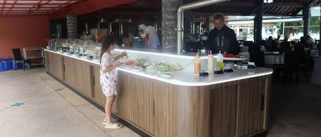 A buffet counter with a wooden finish, a person serving food, and a counter with various dishes and condiments.