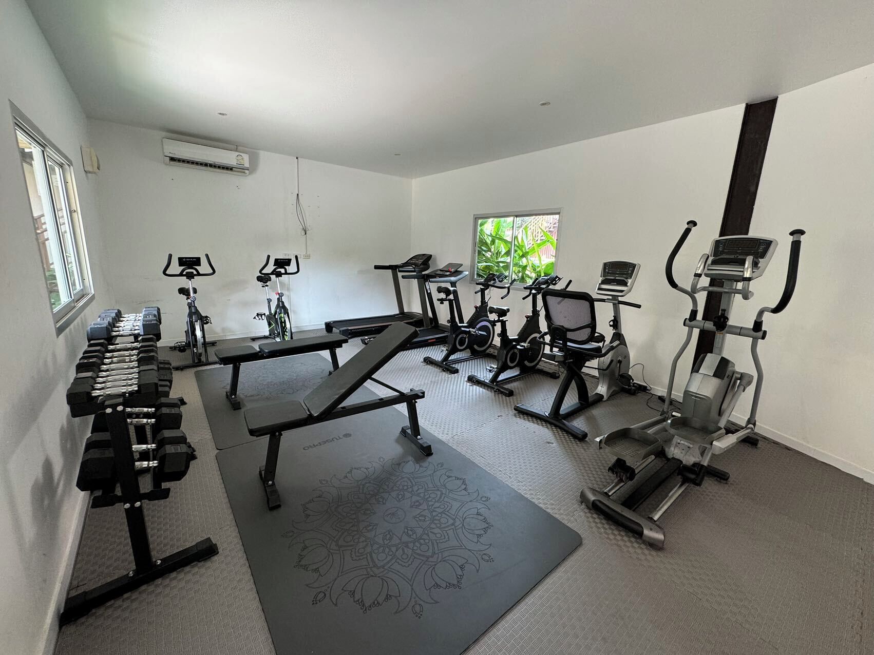 A gym with various exercise equipment including dumbbells, benches, treadmills, and stationary bikes.