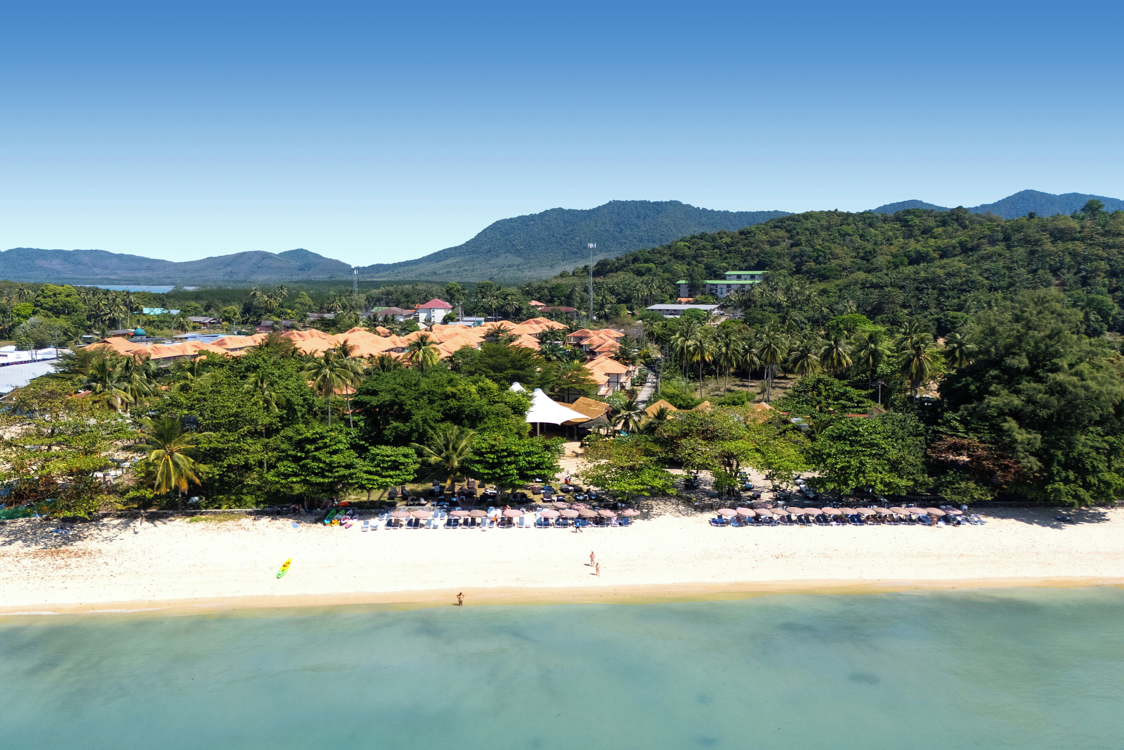 Una platja amb sorra, palmeres i muntanyes al fons.